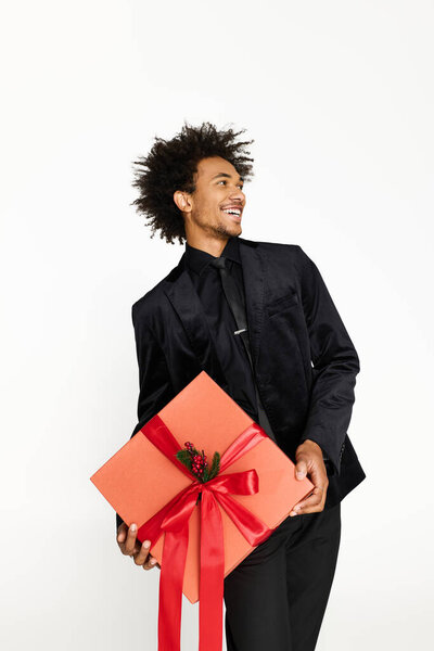 Elegant young man smiles widely while holding a large gift with a red bow.