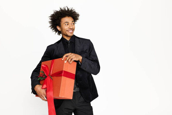 A young man in stylish attire showcases a beautifully wrapped gift with a bright smile.