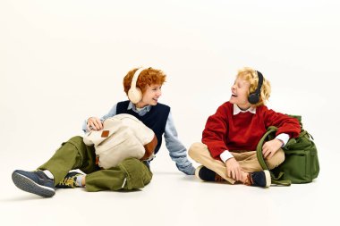 İki çocuk temiz beyaz bir zeminde oturmuş, kulaklık takıp kahkaha ve müzik dinliyorlar..