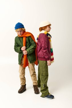 İki çocuk arka arkaya renkli kış kıyafetleri ve neşeli ifadeler sergiliyor..