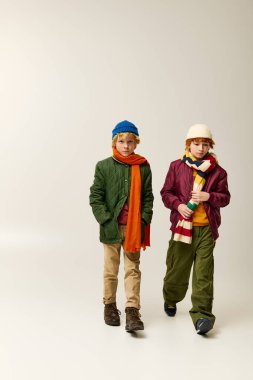 Ilık giyinmiş iki modacı çocuk güvenli bir şekilde geziniyor, neşeli kış moda tercihlerini sergiliyorlar..