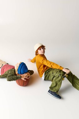 İki çocuk yerde rahatlıyor, biri basketbol topunu tutuyor, oyuncu tarzlarını sergiliyor..