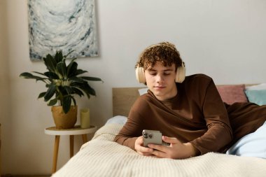 Kıvırcık saçlı bir genç rahat odasında, kulaklıkla müzik dinliyor..