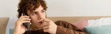 Kıvırcık saçlı bir genç, modern yatak odasında telefon konuşmasından hoşlanıyor.