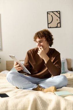 Genç çocuk, şık bir yatak odasıyla çevrili iken yatağında oturup tablet okuyor..