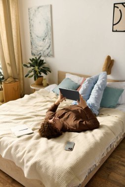 Kıvırcık saçlı ergen, rahat bir yatak odasında, yatakta yatarken tablet kullanmaktan hoşlanıyor..