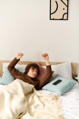 Kıvırcık saçlı bir genç yatakta uzanıyor, rahat odasında dinleniyor..