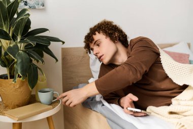 Kıvırcık saçlı genç bir çocuk, yatakta uzanırken fincanına uzanır ve sessiz bir sabah geçirir..