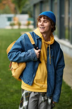 Kıvırcık saçlı neşeli bir genç bu sonbahar mavi bereli ve kot ceketli poz veriyor..