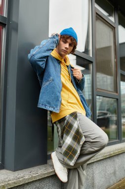 Kıvırcık saçlı genç bir çocuk serin bir sonbahar gününde mavi bir bere ve kot ceket giyer..