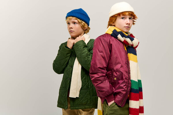Два мальчика стоят спиной к спине в яркой зимней одежде, демонстрируя свои уникальные стили в помещении.