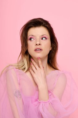 Göz alıcı pembe makyajlı genç bir kadın yumuşak renklerle dolu bir stüdyoda zarifçe poz veriyor..
