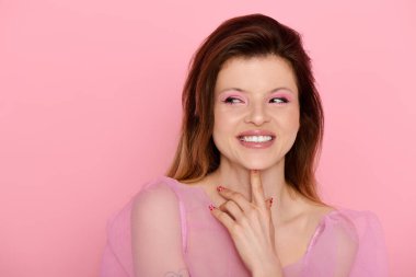 Güzel, genç bir kadın neşeli bir gülümsemeyle poz veriyor. Pembe bir makyaj ve düz bir bluz giyiyor..