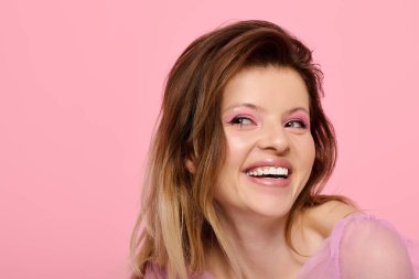 Parlak bir stüdyoda genç bir kadın pembe makyaj malzemesi ve pırıl pırıl bir bluzla hava atıyor..