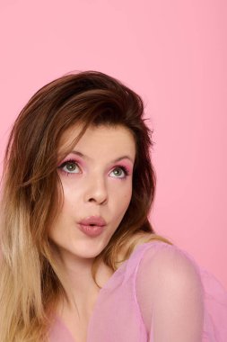 Genç bir kadın pembe renkli canlı bir makyaj ve yumuşak pembe bir arka plana karşı katıksız bir bluz sergiliyor..