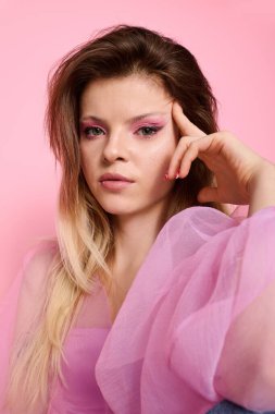 Kendine güvenen genç bir kadın, modaya uygun pembe makyajlı ve katıksız bluzlu bir stüdyoda poz veriyor..