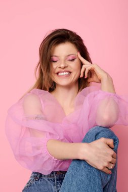 Stüdyoda gülümseyen genç bir kadın pembe makyajını ve saf organza bluzunu sergiliyor..