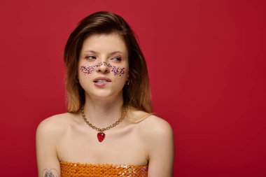 Parlak makyajlı ve çıplak omuzlu genç bir kadın cesur bir kırmızı arka plana karşı poz veriyor..