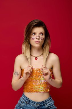 Genç bir kadın ışıl ışıl makyajını ve şık kıyafetlerini canlı bir stüdyo arkaplanında sergiliyor..