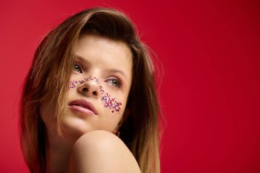 Parlak makyajlı genç bir kadın renkli bir stüdyo ortamında zarif pozlar veriyor..