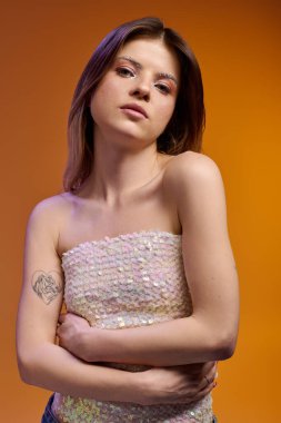 Moda kıyafetli çekici genç kadın, ışıl ışıl makyajını sıcak bir arka planda öne çıkarıyor..