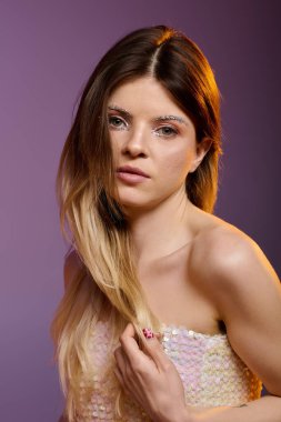 Kendine güvenen genç bir kadın, parlak makyajını ve çıplak omuzlarını stüdyoda gösterir..