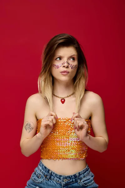 Genç bir kadın ışıl ışıl makyajını ve şık kıyafetlerini canlı bir stüdyo arkaplanında sergiliyor..