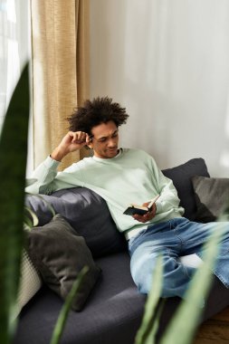 Yakışıklı genç adam şık bir oturma odasında telefonunu kontrol ederken rahat bir kanepede dinleniyor..