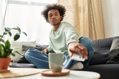 Genç, yakışıklı bir adam rahat bir oturma odasında arkasını yaslar ve rahatlarken bir şeyler içer..