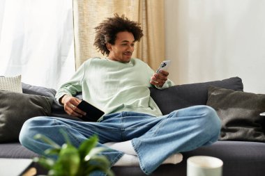 Genç bir Afrikalı Amerikalı rahat bir şekilde rahat bir koltukta oturuyor, akıllı telefonunu karıştırıyor..