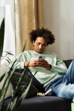 Genç ve yakışıklı bir adam, rahat ve modern bir evde, bir kanepede rahat bir şekilde telefonunu kullanıyor..