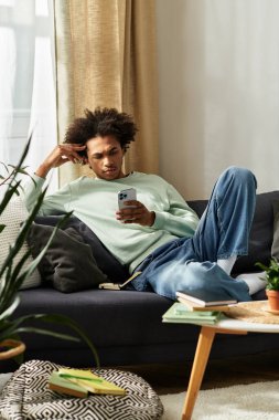 Yakışıklı bir Afrikalı genç Amerikalı, akıllı telefonunu kullanırken rahat ve modern evinde dinleniyor..