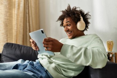 Genç bir adam rahat bir kanepede rahatlar, rahat bir yerde tabletiyle meşgul olurken gülümser..