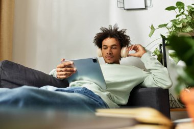 Yakışıklı genç adam evinde rahatça uzanıyor, tabletten müzik dinliyor..