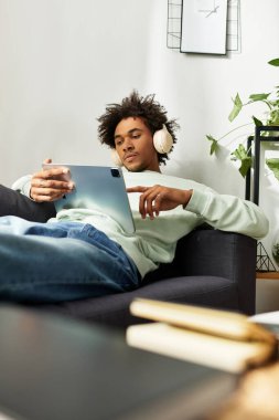 Şık, genç ve güçlü bir adam kanepede uzanır, tabletini kullanır ve müzikten zevk alır..