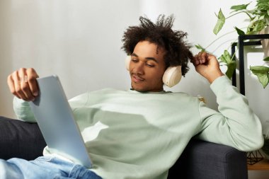 Genç adam kanepede dinleniyor, müzikten zevk alıyor ve rahat evindeki tablette geziniyor..