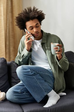 Genç adam evde rahatlamış, telefonda konuşurken kahvenin tadını çıkarıyor, rahat bir havayı kucaklıyor..