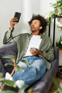 Yakışıklı, Afro-Amerikan bir adam modern evinde rahatlıyor, cihazına odaklanıyor..