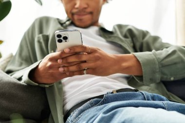 Genç, yakışıklı Afrikalı Amerikalı bir adam modern evinde, akıllı telefonuyla meşgul..