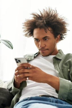 Yakışıklı, Afro-Amerikan bir adam evinde rahatlıyor, dikkatle akıllı telefonuna odaklanıyor..