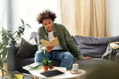 Yakışıklı bir Afrikalı genç Amerikalı adam evdeki kanepesinde rahatça otururken kitap okuyor..