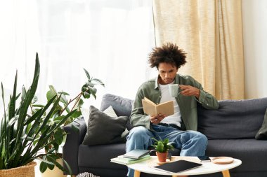 Genç, yakışıklı bir Afro-Amerikan erkeği evinde rahatça oturup kitap okurken bir yudum içki içiyor..