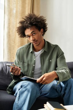 Doğal bukleli yakışıklı genç adam evinde rahat oturur, defterine yazmaya odaklanır..