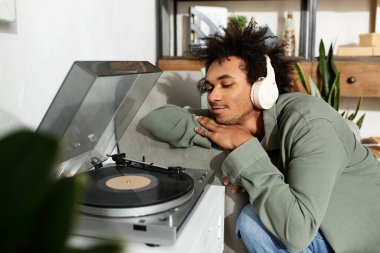 Genç yakışıklı bir adam plakları dinliyor, rahat evinde müziğe dalmış..