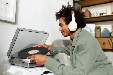 Genç Afrikalı Amerikalı adam rahat yaşam alanında dinlenirken vinil müzik dinliyor..