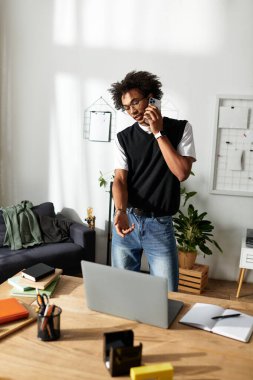 Genç bir Afro-Amerikalı adam, modern bir masada çalışırken telefonuyla konuşuyor..