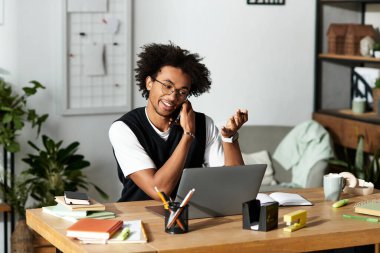Genç Afrikalı Amerikalı bir adam masasında çalışırken bir telefon görüşmesi yapıyor..
