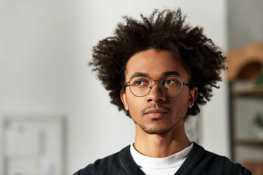 Kıvırcık saçlı ve gözlüklü genç Afro-Amerikan erkeği evinde sıcak, davetkar bir atmosfer yaratıyor..