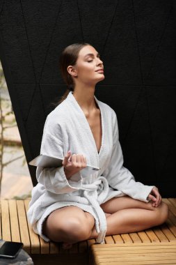 Rahat bir bornoz giymiş genç bir kadın spa günü boyunca huzurlu bir anın tadını çıkarıyor..