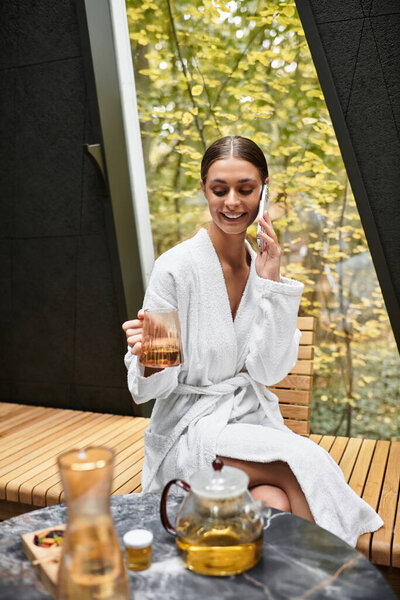 Young woman in a white bathrobe enjoys herbal tea while relaxing at a contemporary spa.